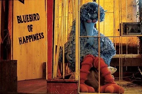 A yellow-painted doorway beneath a hand-lettered sign reading "Bluebird of Happiness", with a large blue feathered figure seated inside.