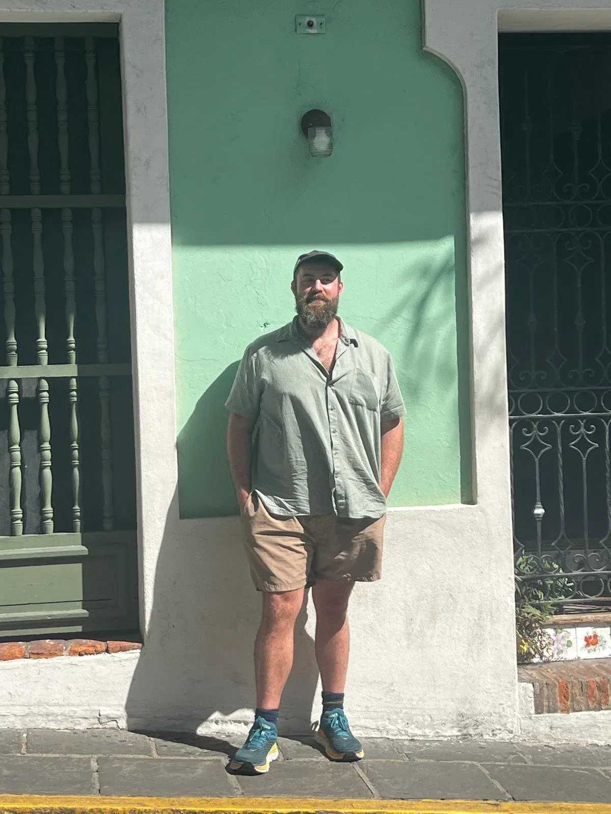 A man standing against a green-painted colonial house front with black iron window grilles.