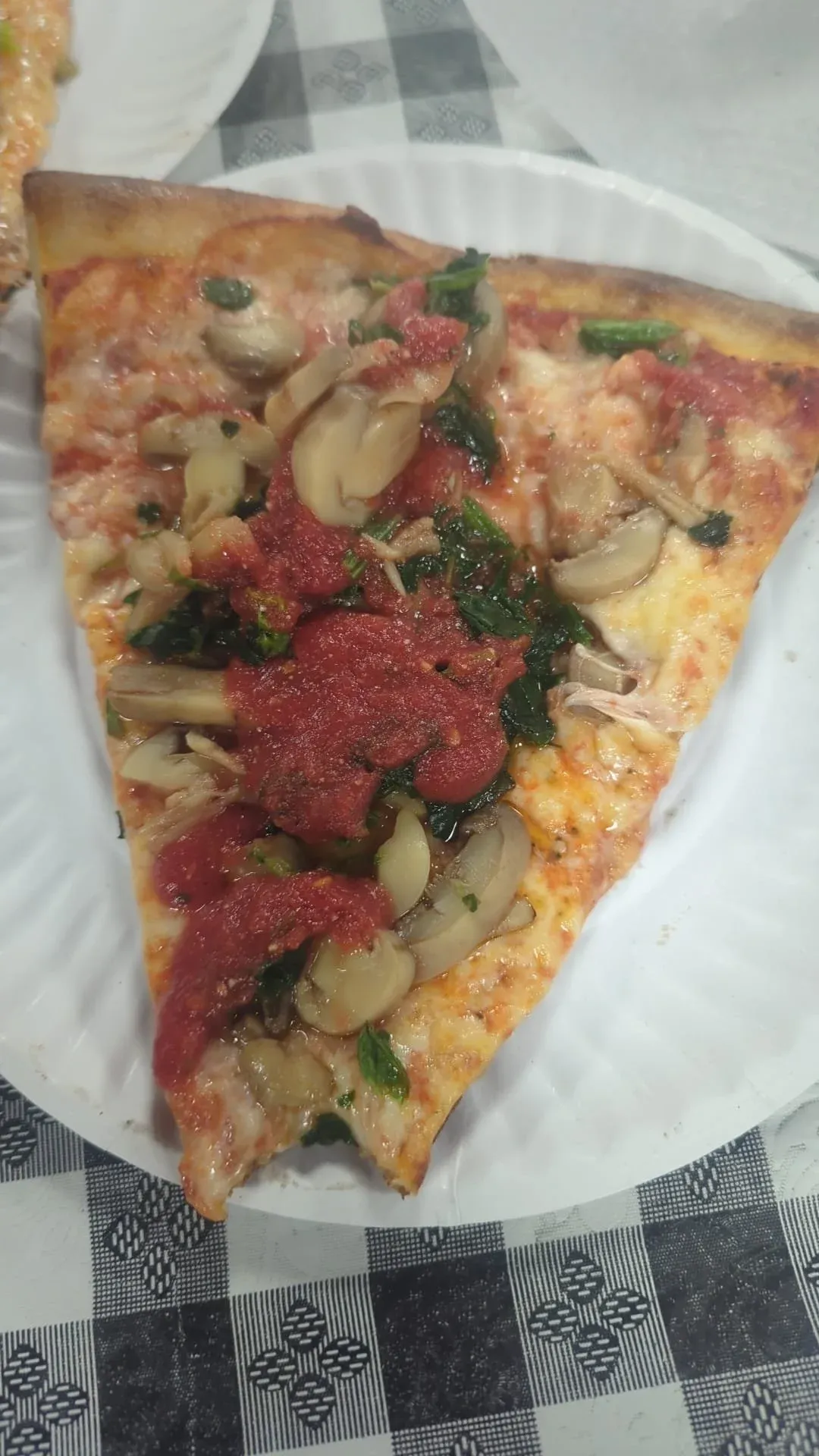 A slice of pizza on a paper plate, photographed from above on a chequered cloth.