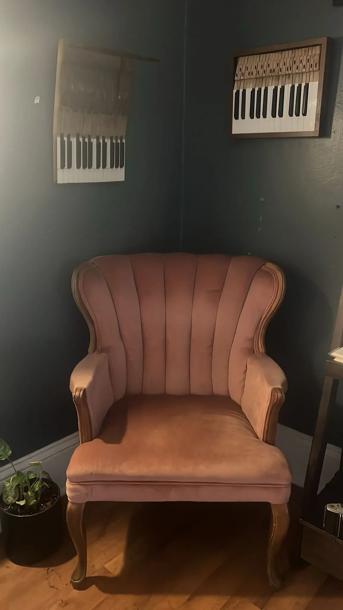 A pink velvet armchair in a dark green room, framed prints of keyboards on the wall above it.