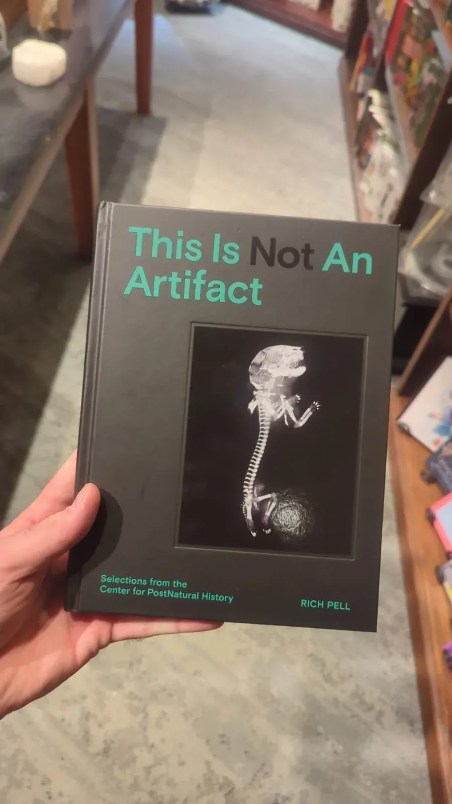 Hands holding a book titled "This Is Not An Artifact" with an X-ray image on its cover.