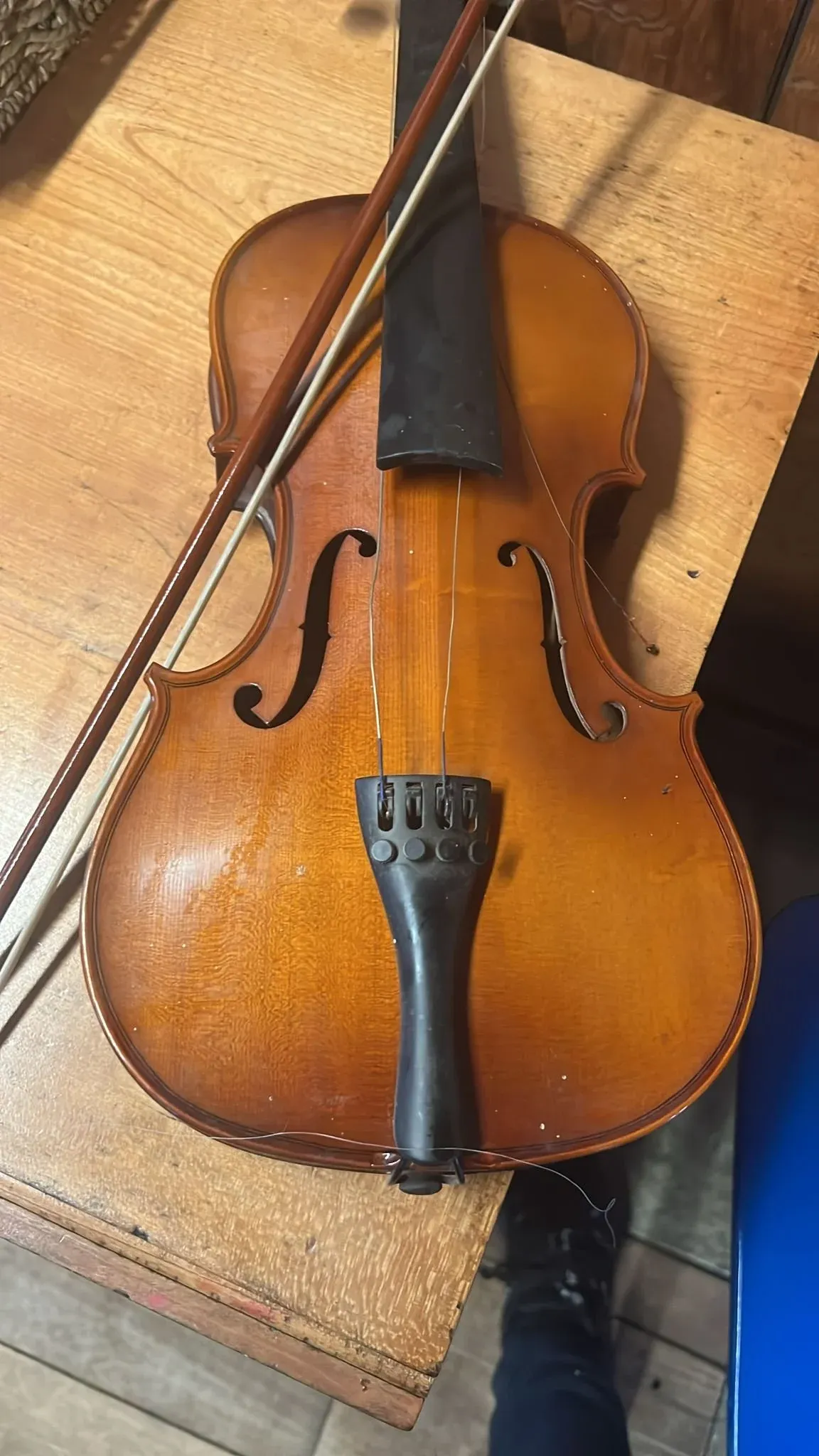 A violin and bow lying together on a bare wooden floor.