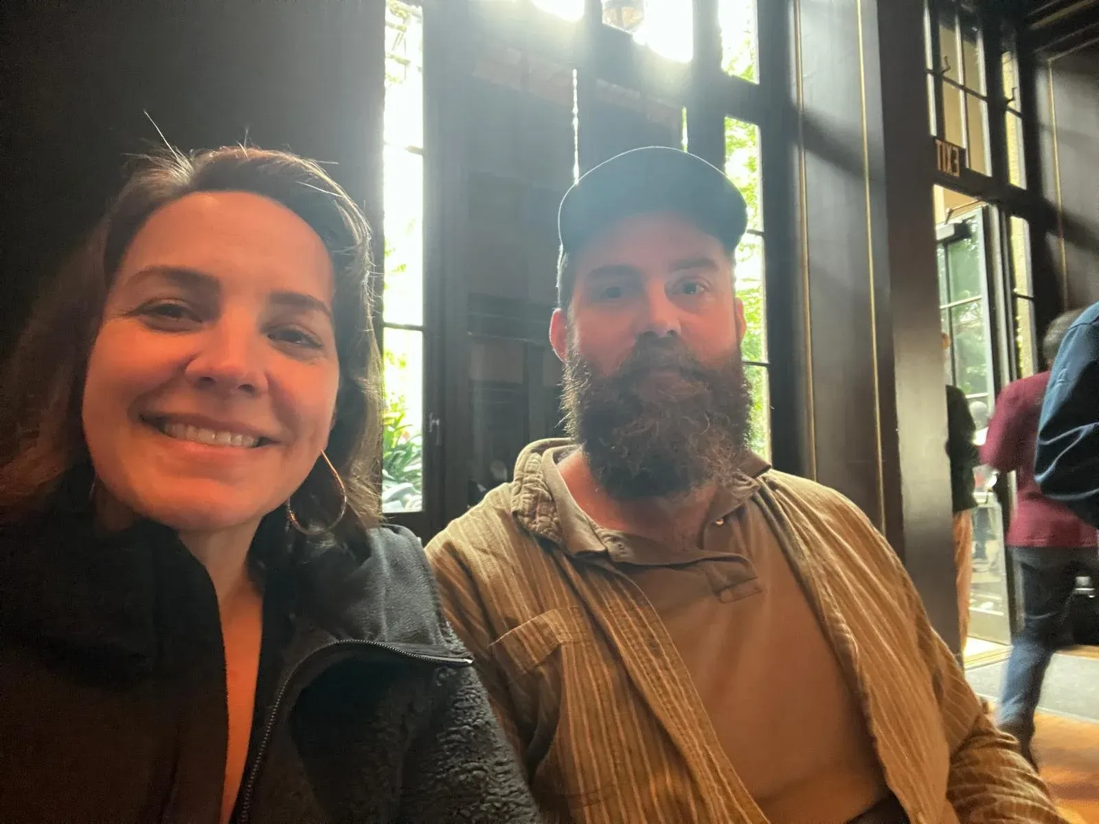 A woman and a bearded man photographed together in bright window light.
