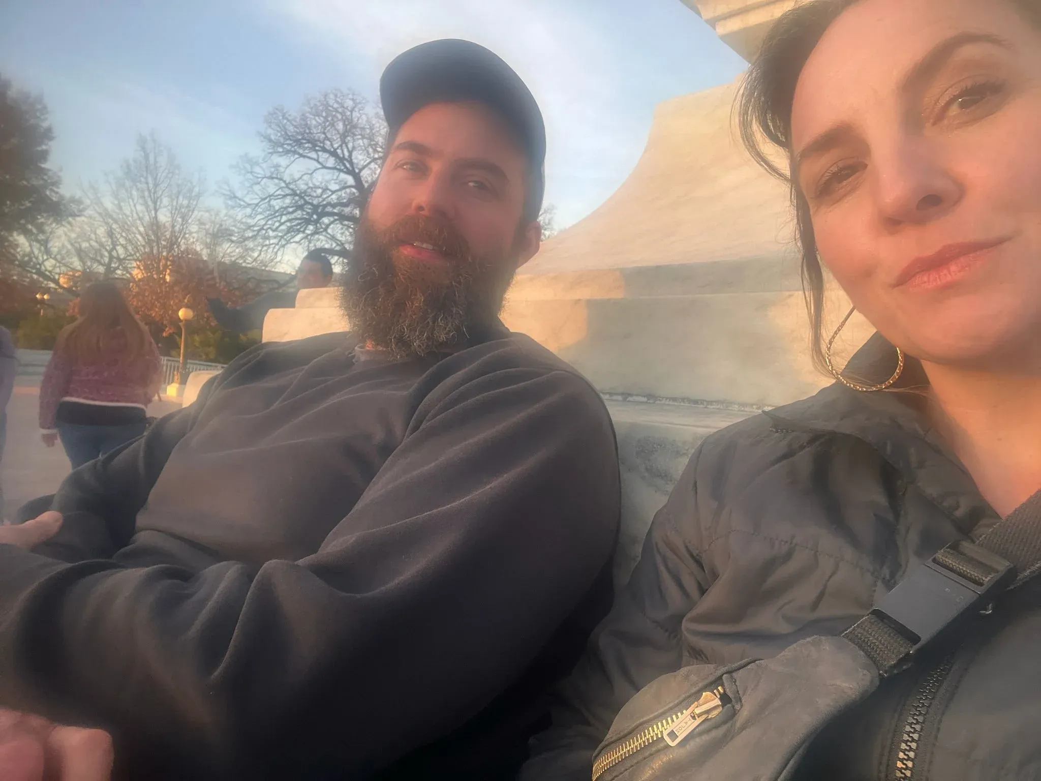 A bearded man and a woman photographed close together in a car at golden hour.