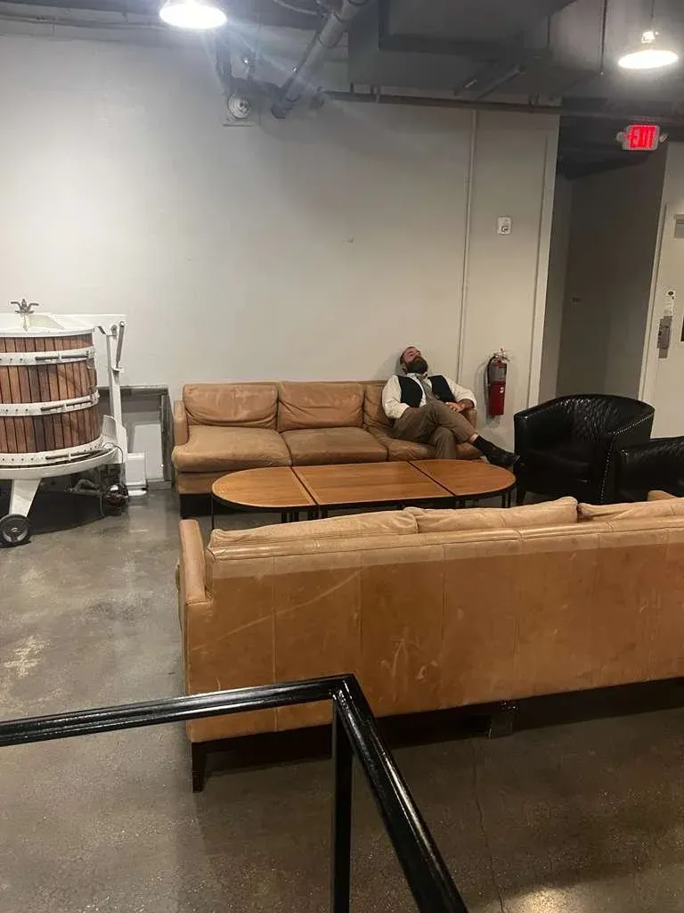 An empty loft space with a leather sofa, a dog asleep on it, and a large wooden press in the corner.