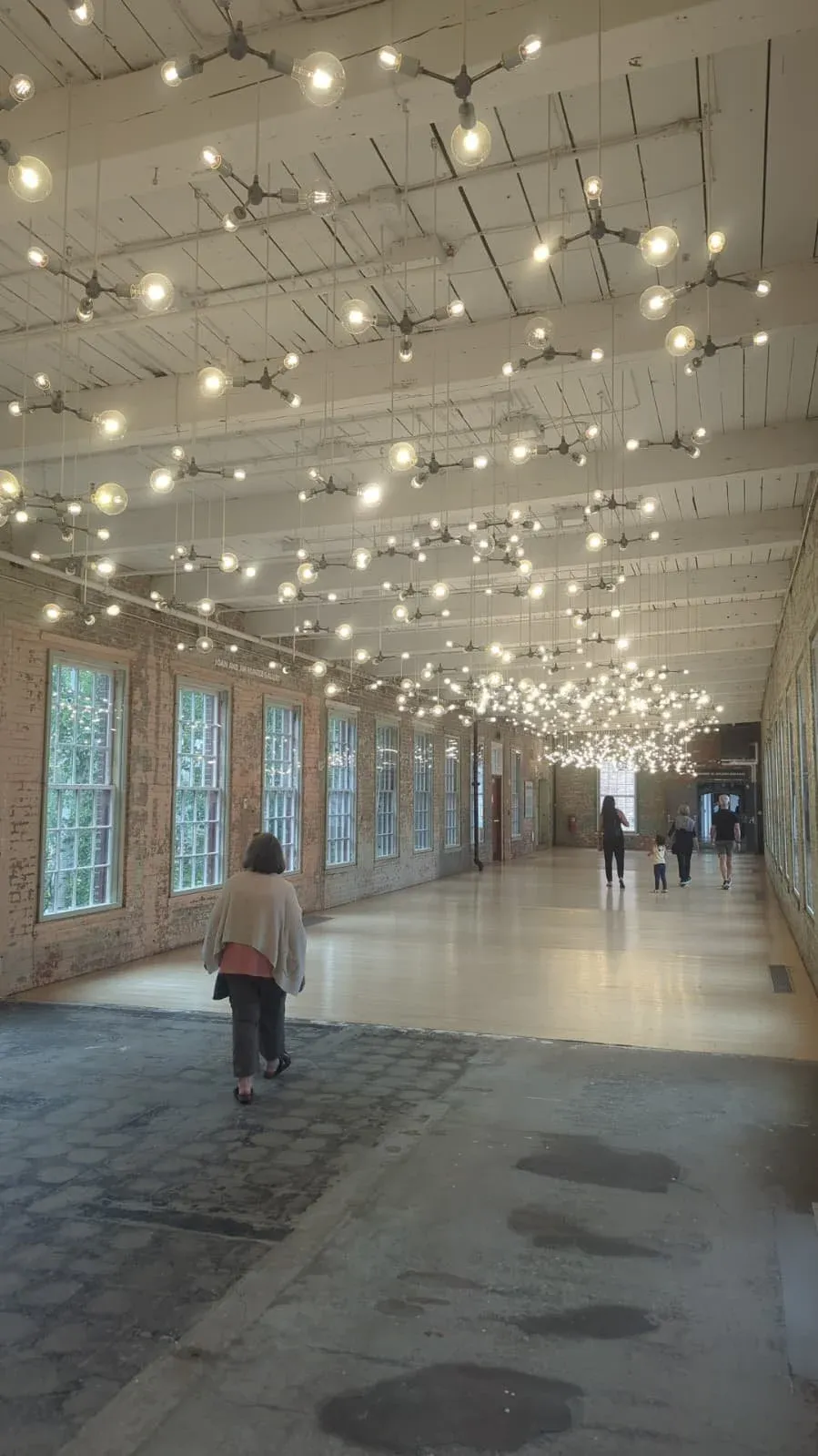 A long white corridor strung end to end with festoon lights, a single figure walking away.