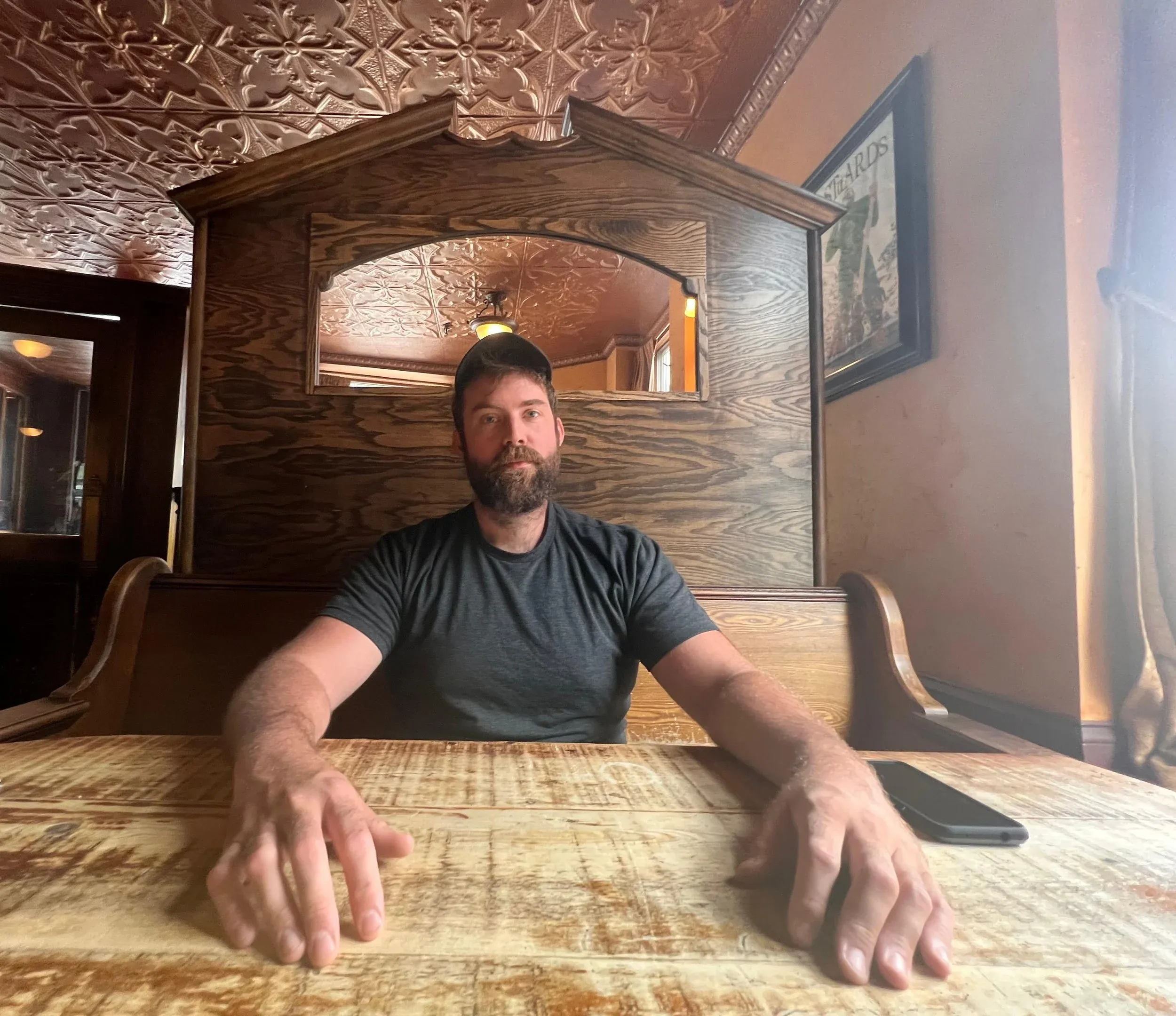 A man seated at a long table beneath a carved wooden canopy, a pressed-tin ceiling overhead.