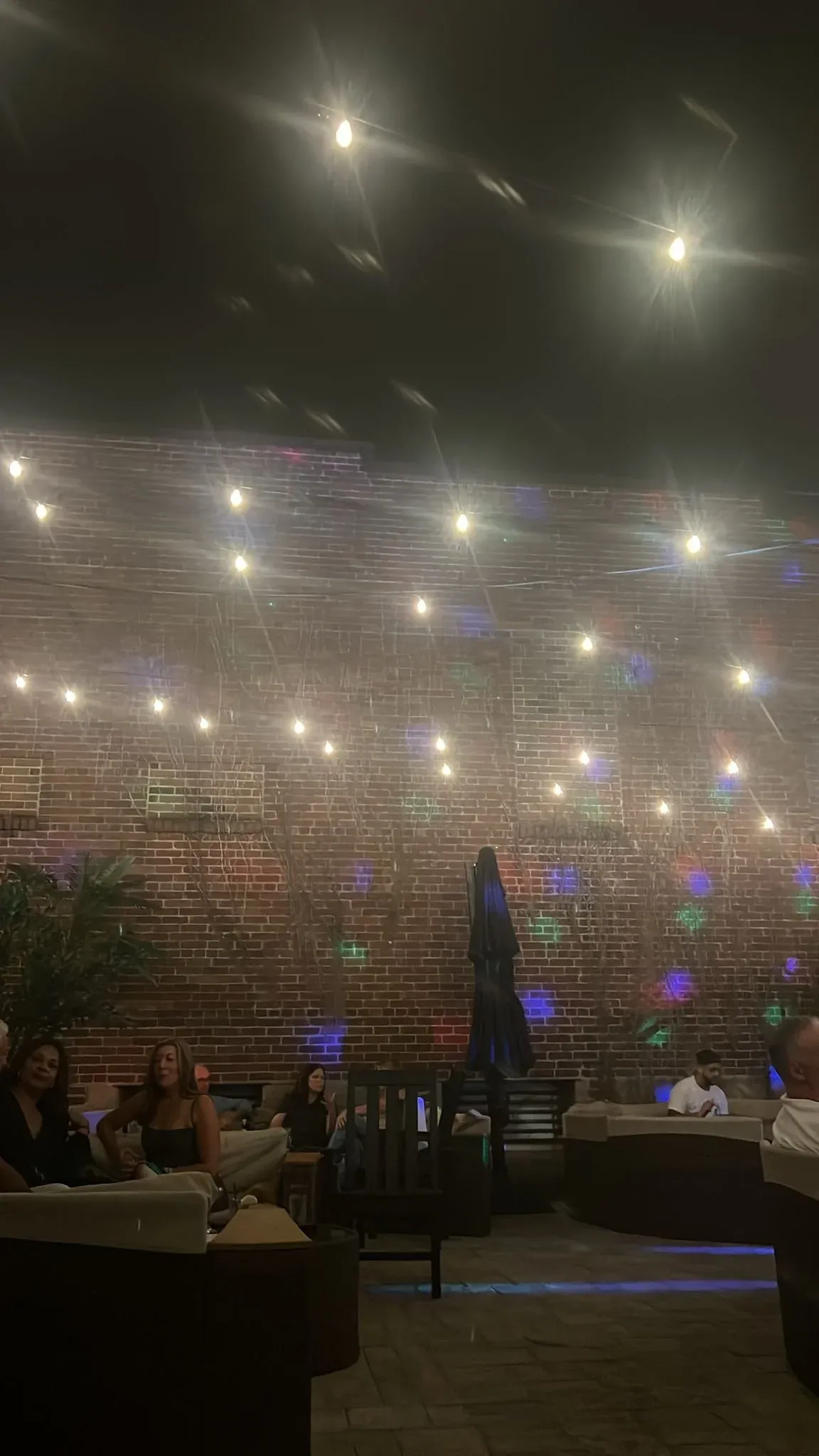 Festoon lights strung above an outdoor courtyard at dusk, tables below.