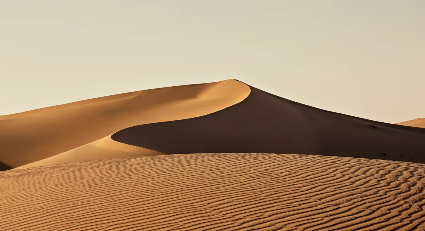 A single sand dune under a pale sky, its crest cutting a clean diagonal.